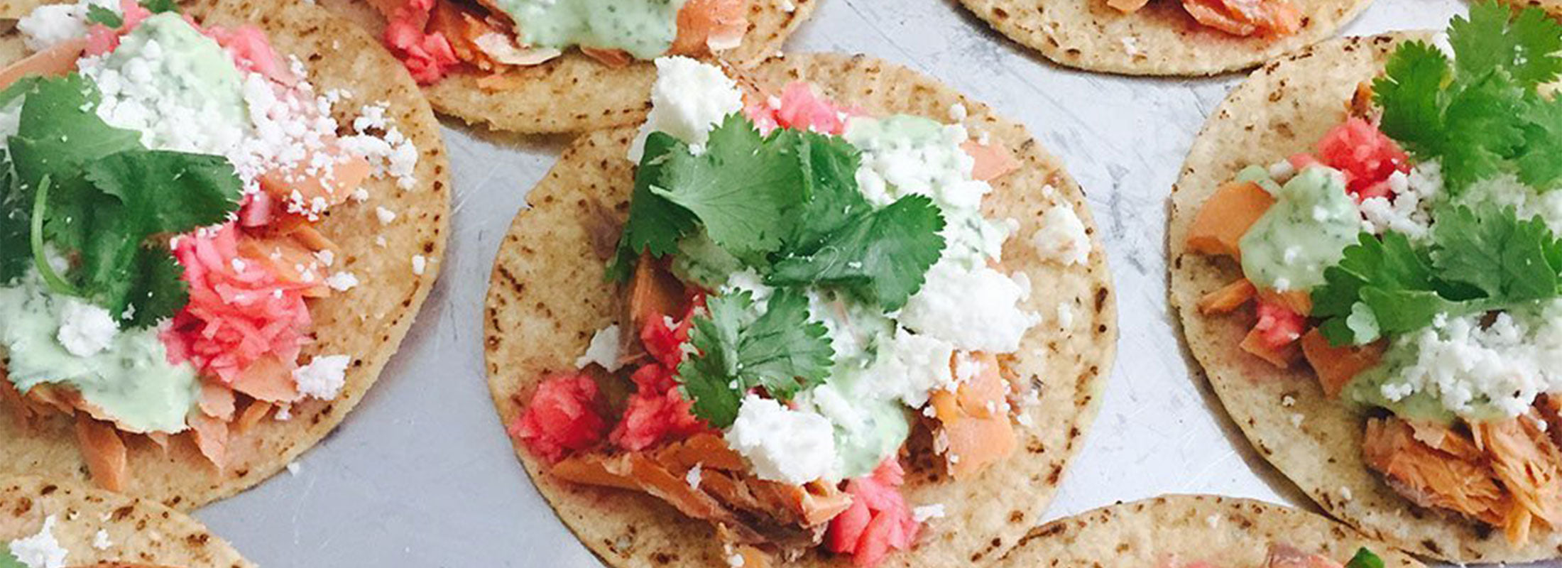 A tray of open tostadas, filled with Patagonia Provisions Wild Sockeye Salmon, cheese, sauce, and cilantro